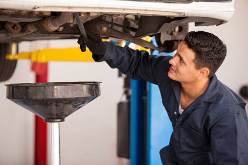 Young Hispanic mechanic draining engine oil from a car for an oil change at an auto shop